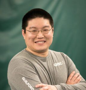 A man wearing glasses and a grey shirt with the word guilford on it