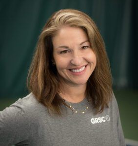 A woman wearing a gray shirt with the word grsc on it is smiling.