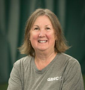 A woman wearing a gray shirt is smiling for the camera.