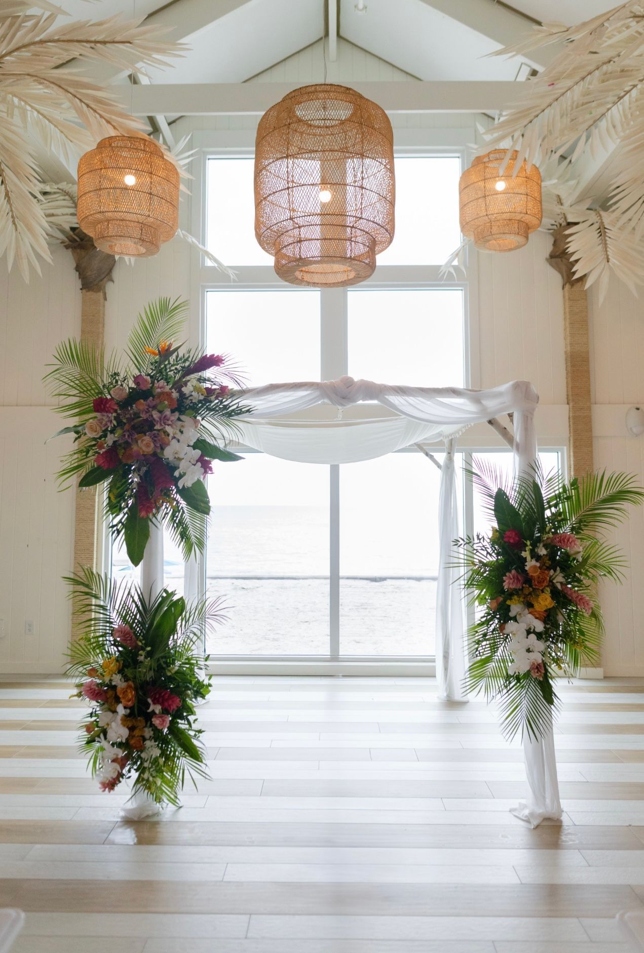 Gold floral arch on a sandy beach with the ocean and blue sky in the background.