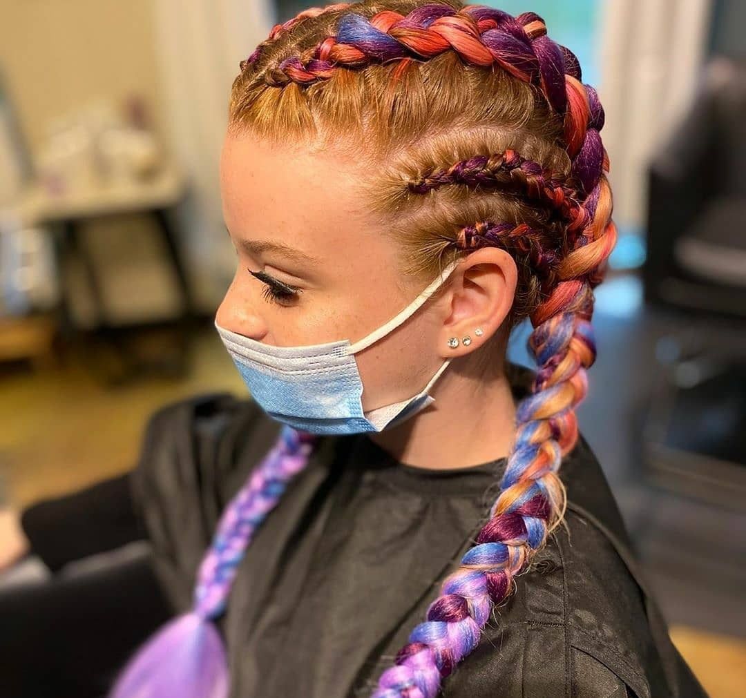 Side profile of a person wearing a blue surgical mask and a hairstyle featuring multiple colorful, braided cornrows.