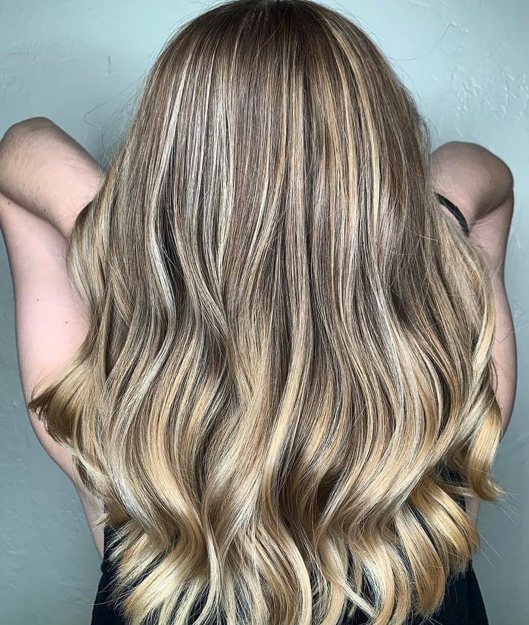 A person with long, wavy blonde highlighted hair styled with a crimped texture, viewed from behind.