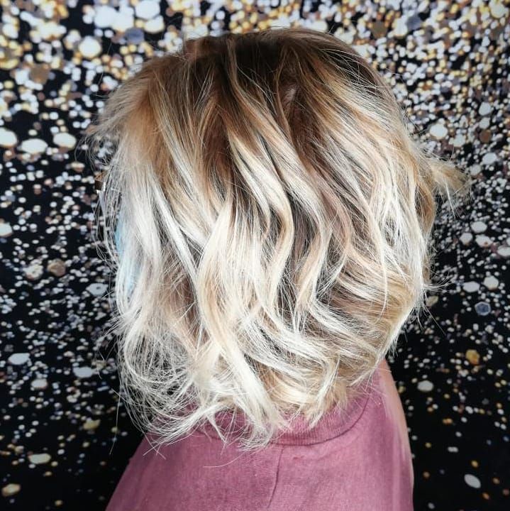 Wavy, shoulder-length hair with a dark brown to platinum blonde ombre color transition against a blurred bokeh background.