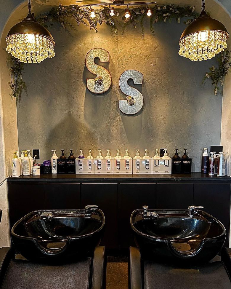 Two black shampoo basins set in front of a dark cabinet with hair products and a wall marked with two large 