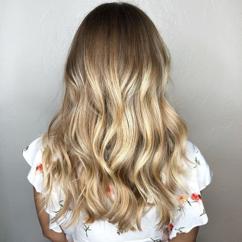 Back view of long, blonde wavy hair with crimped texture, worn by someone in a white floral top against a plain wall.
