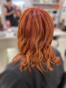Back view of shoulder-length, wavy hair with vibrant copper-red tones in a salon setting.