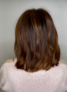 A view from behind of shoulder-length, wavy brown hair with warm highlights, worn by someone in a light sweater.