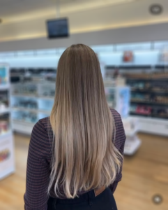 A person with long, straight hair featuring a blonde ombré transition, seen from behind inside a store.