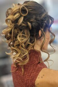 A woman seen from the back wearing a textured rust-colored high-neck top with her hair styled in a voluminous curly updo.