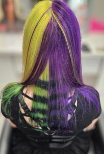 A person with split-dyed hair, featuring vibrant yellow on the left and purple on the right, with green striped undersides.