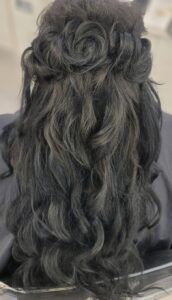 A back view of long, dark, wavy hair styled in a half-updo featuring delicate rosette-shaped curls at the crown.
