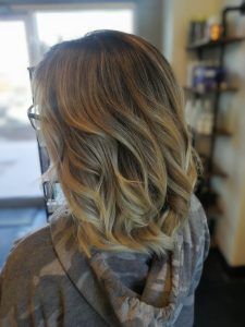 Shoulder-length hair styled in soft, loose waves with highlights, seen from behind in an indoor salon setting.