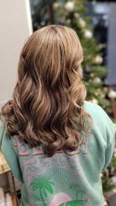 A person with long, wavy, highlighted brown hair, seen from behind, wearing a light green graphic sweatshirt.