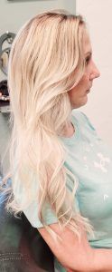 A side profile of a person with long, wavy blonde hair wearing a light blue t-shirt indoors.