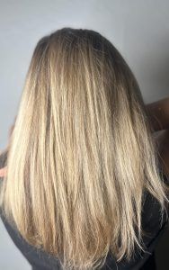 Back view of medium-length, layered blonde hair with lighter highlights, styled straight and smooth.