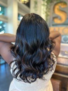 Long, wavy dark hair shown from the back, styled with soft curls in a salon setting.