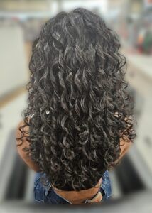 A person from behind displaying long, dark brown, voluminous curly hair that cascades down their back.