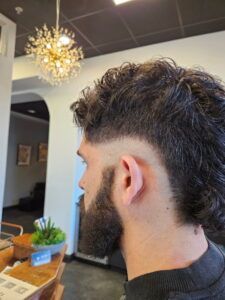 A side profile of a person with a curly-haired mullet and a faded haircut, standing inside a salon.