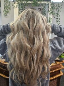 Long, wavy blonde hair with highlights shown from the back, worn by someone in a grey sweatshirt.