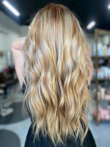 A back view of long, wavy hair featuring highlights and lowlights in shades of blonde, set in a salon.