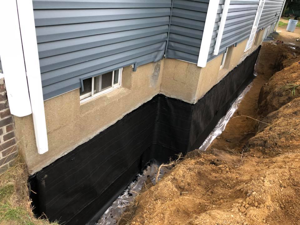 The foundation of a house is being waterproofed with black membrane.