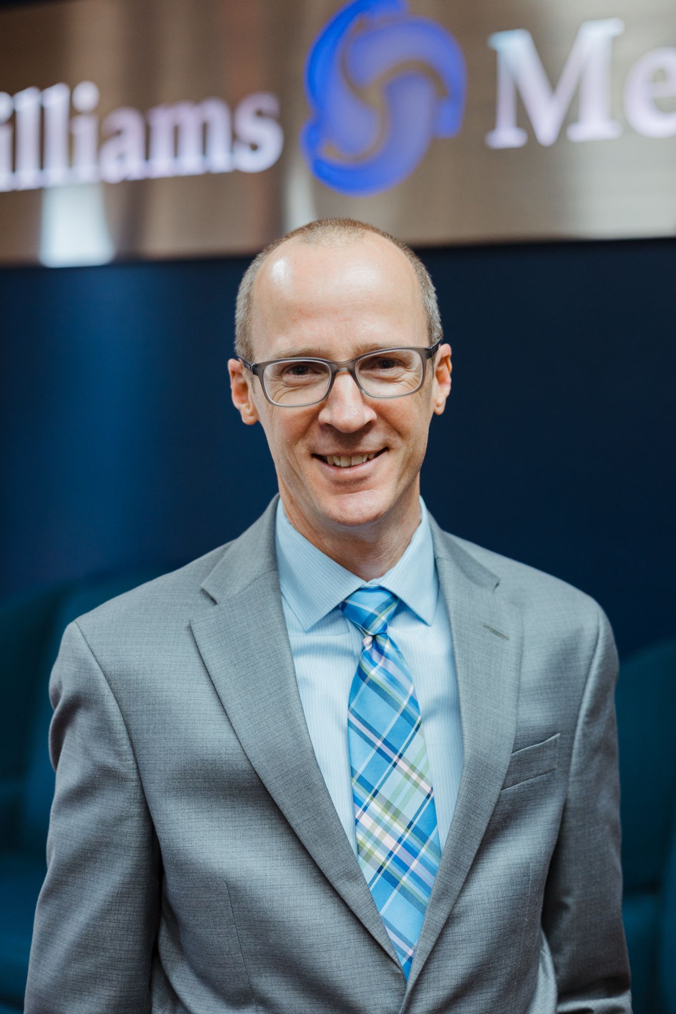 A man in a suit and tie is standing in front of a sign that says williams medical