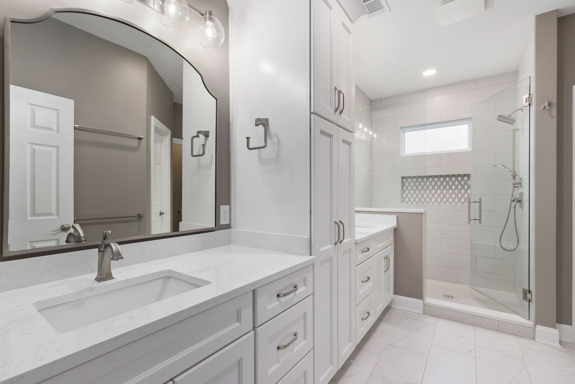 A bathroom with two sinks , a large mirror , and a walk in shower.