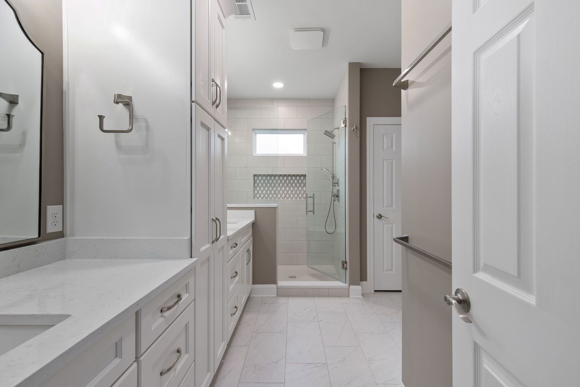 A bathroom with white cabinets and a walk in shower.