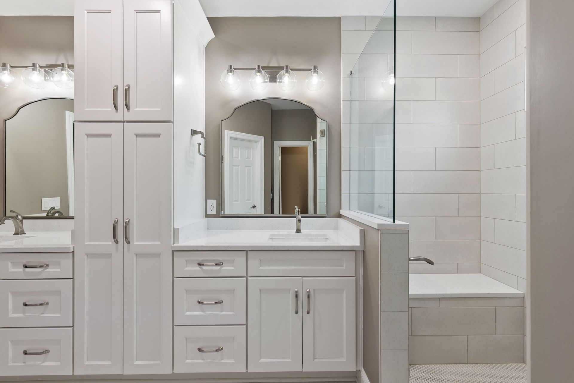 A bathroom with white cabinets , a sink , a mirror and a bathtub.
