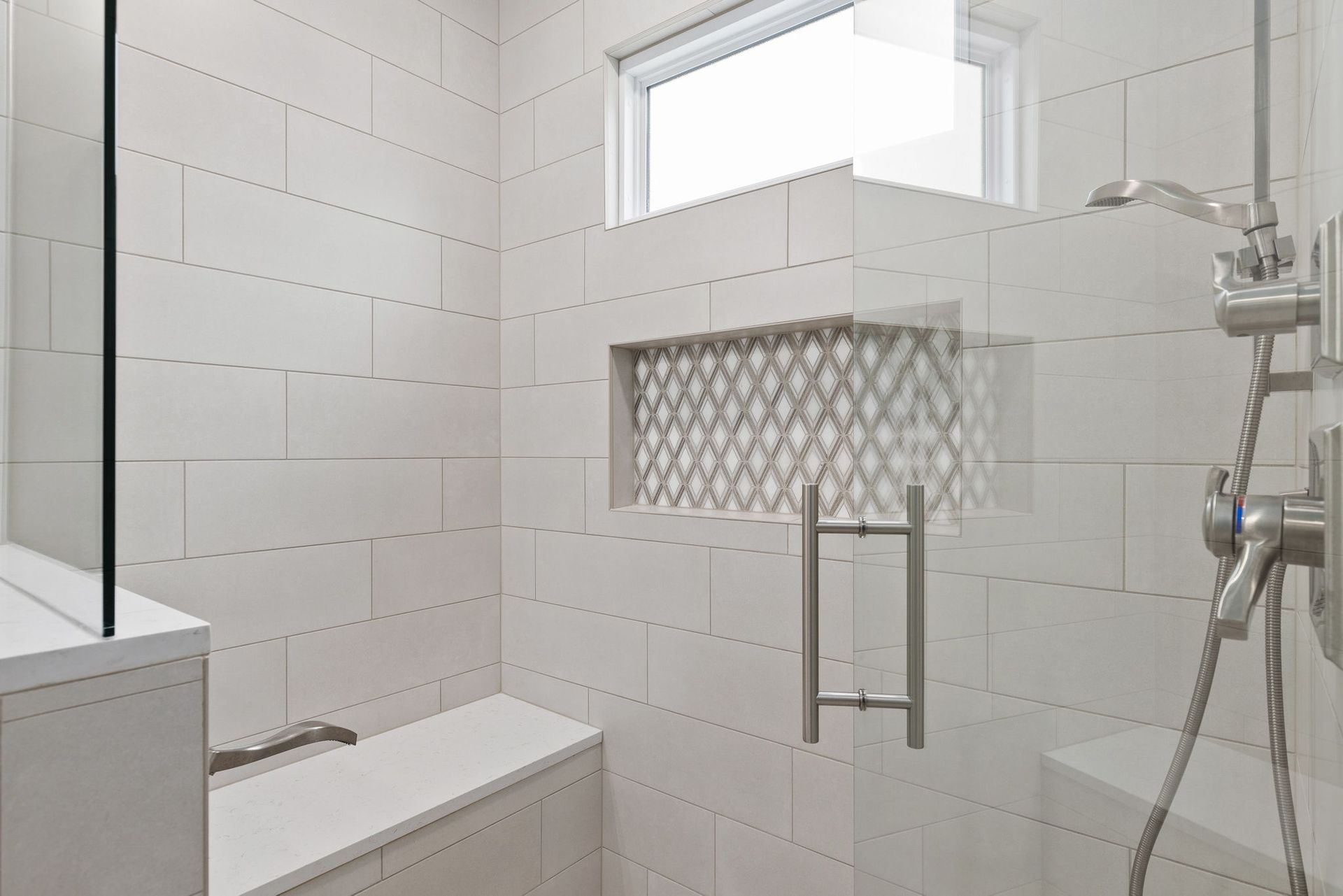 A bathroom with white tiles and a walk in shower with a window.