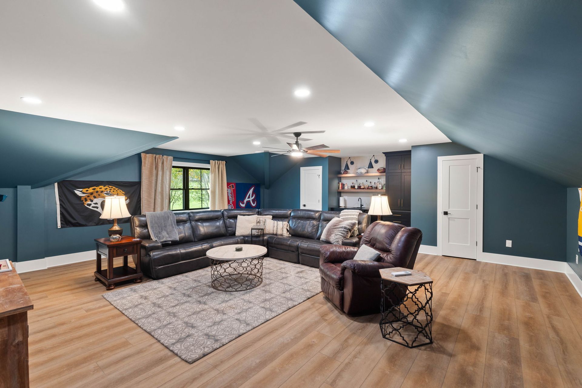 A living room with a large sectional couch , chairs , a coffee table and a ceiling fan.