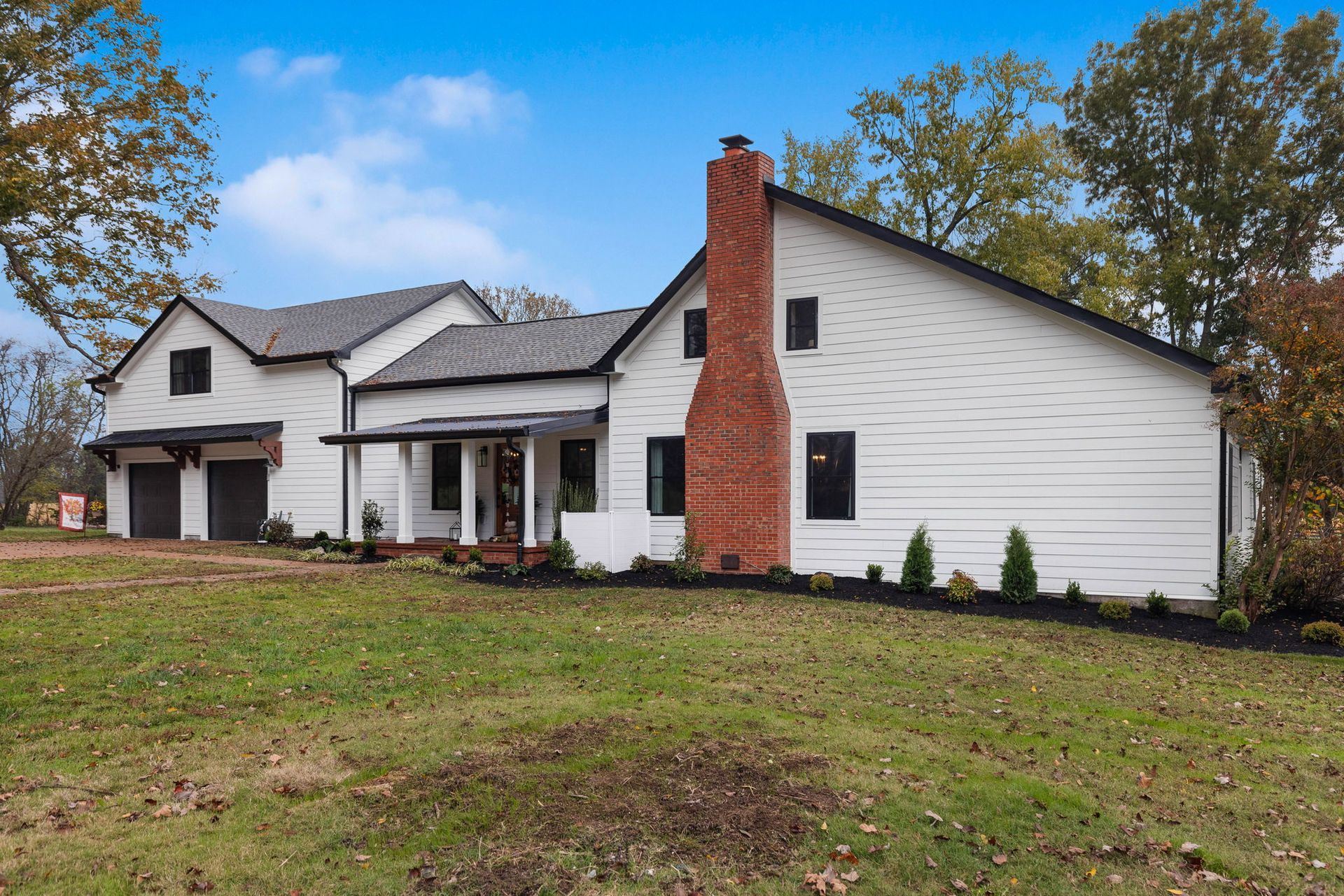 A large white house with a red chimney is sitting on top of a lush green field.