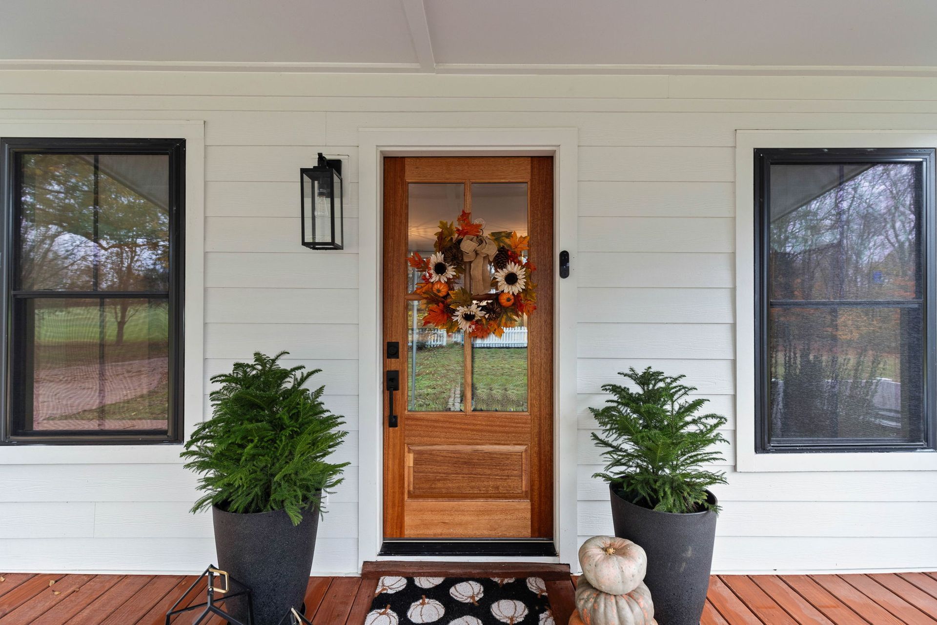 The front door of a house with a wreath on it and potted plants on the porch.