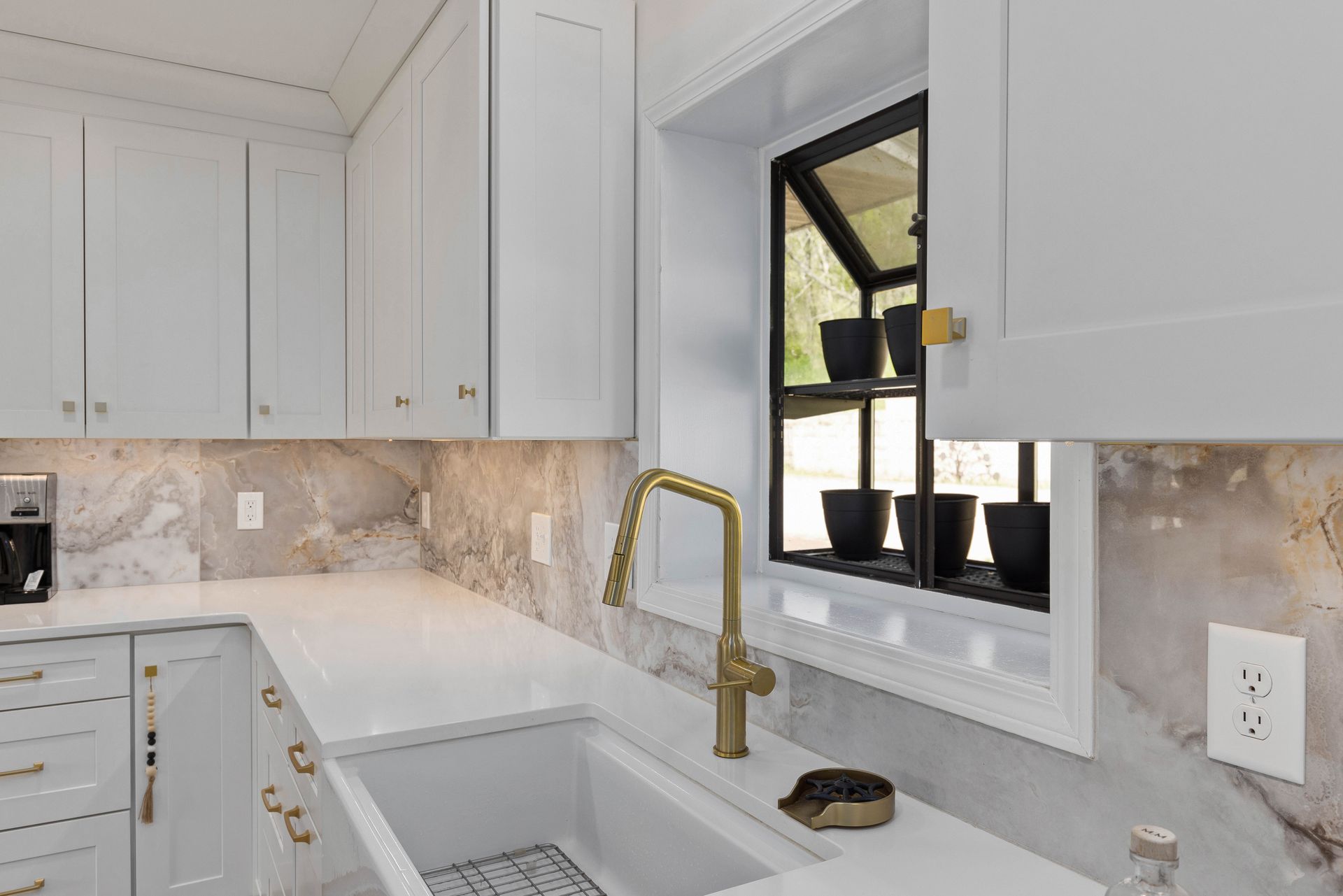 A kitchen with white cabinets , a sink , and a window.