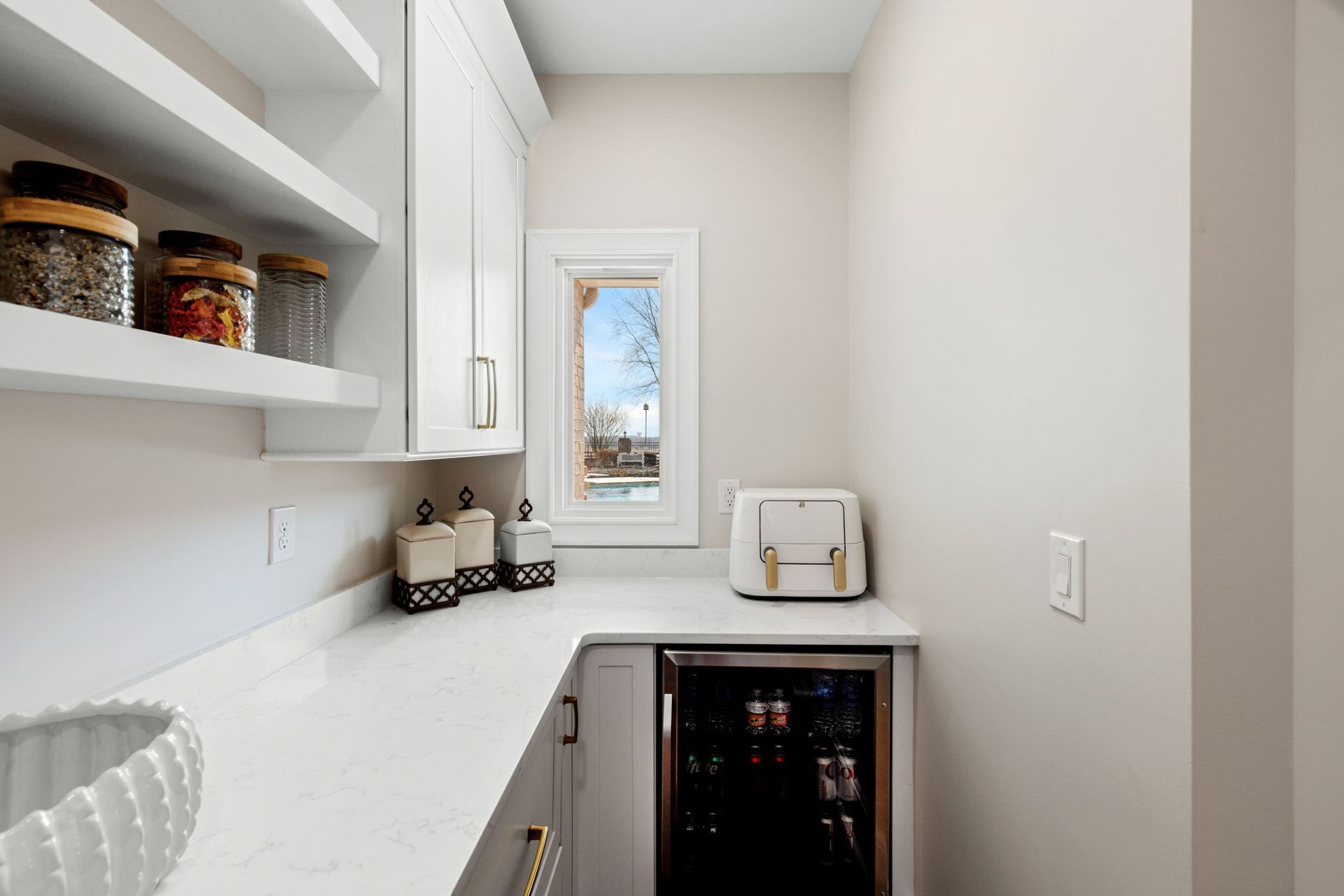 A kitchen with white cabinets , a refrigerator , a toaster oven , and a window.