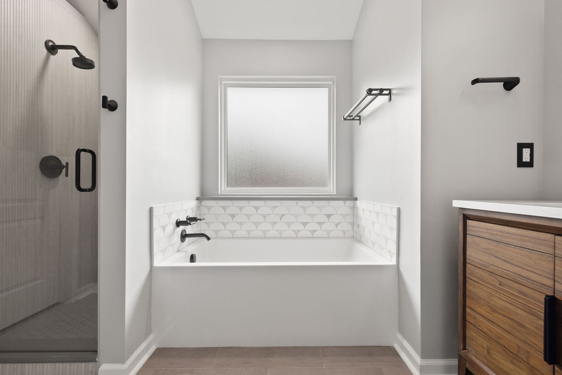 A bathroom with a tub , sink , shower and window.