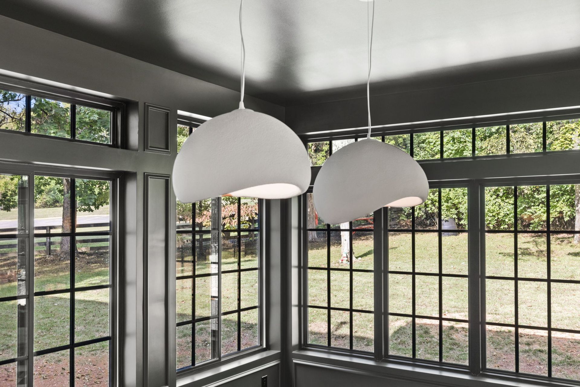 Two white pendant lights are hanging from the ceiling in a room with lots of windows.