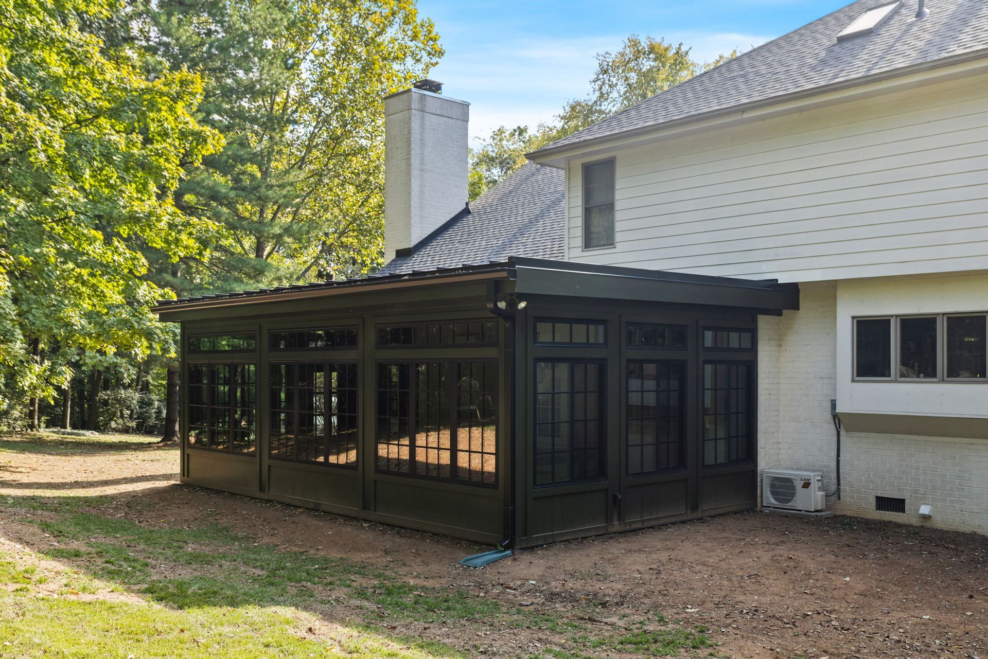 The back of a house with a screened in porch and a chimney.