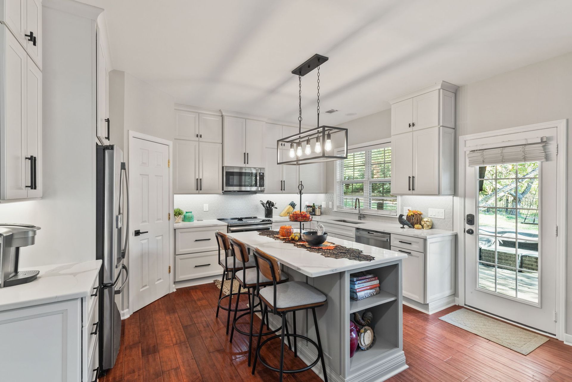 A kitchen with white cabinets , stainless steel appliances , a large island , and hardwood floors.