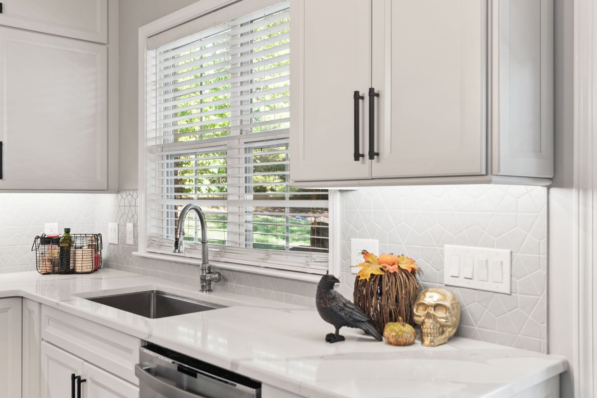 A kitchen with white cabinets , a sink , a dishwasher and a window.