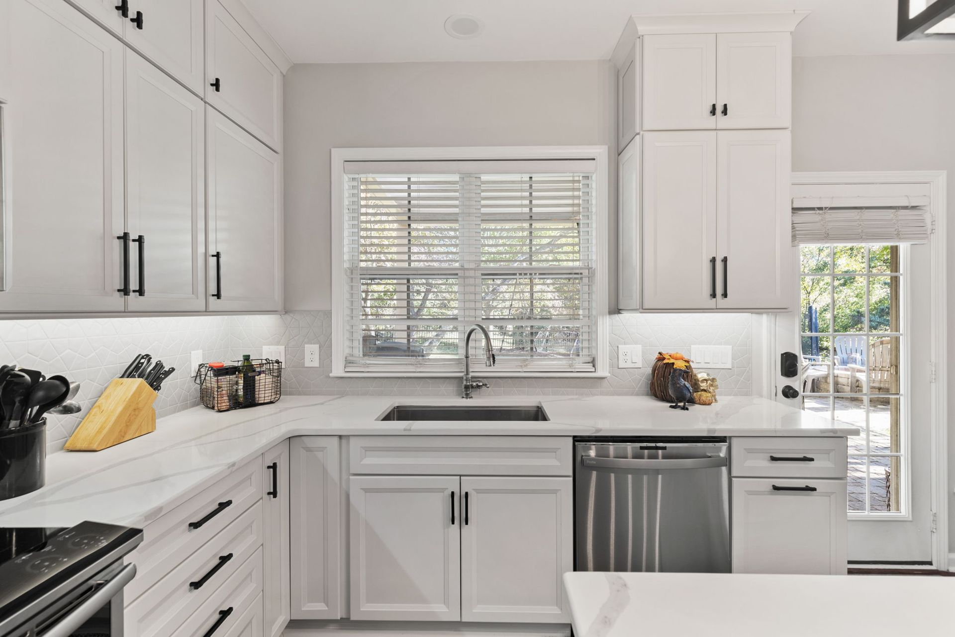 A kitchen with white cabinets , stainless steel appliances , a sink , and a window.