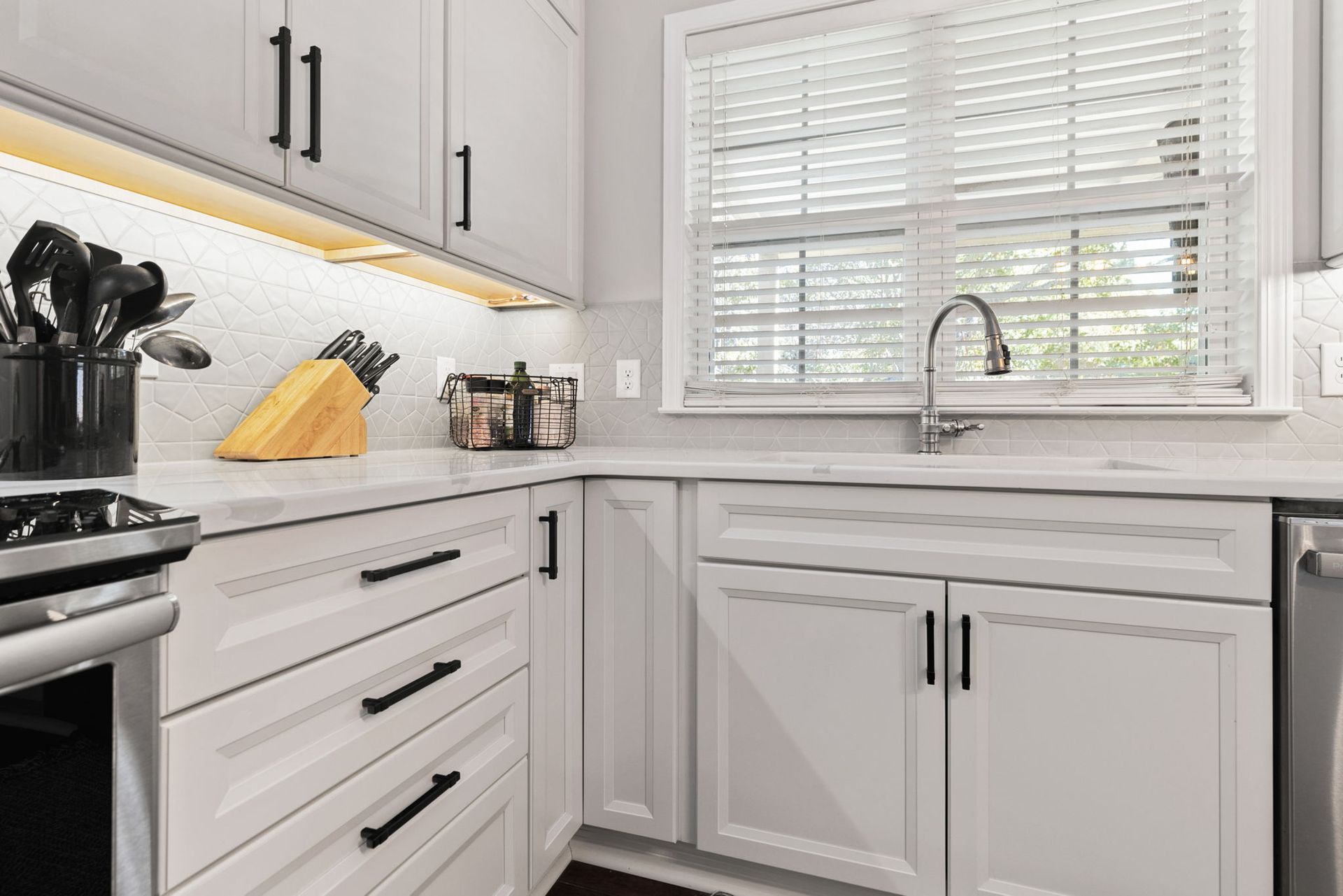 A kitchen with white cabinets , a stove , a sink , and a window.