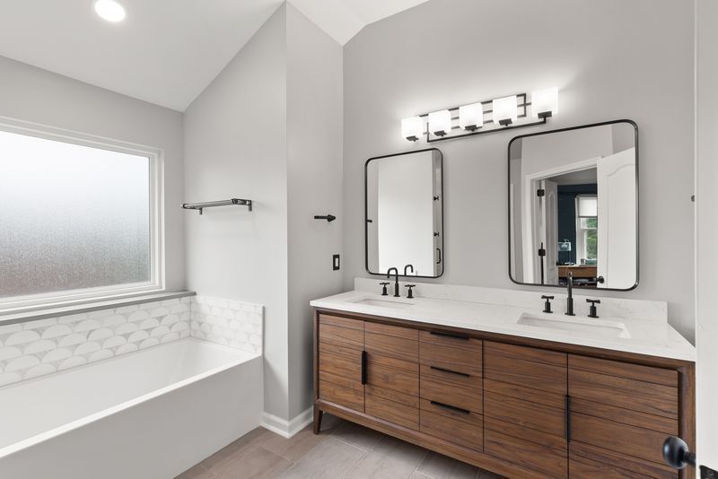 A bathroom with two sinks , a tub and two mirrors.
