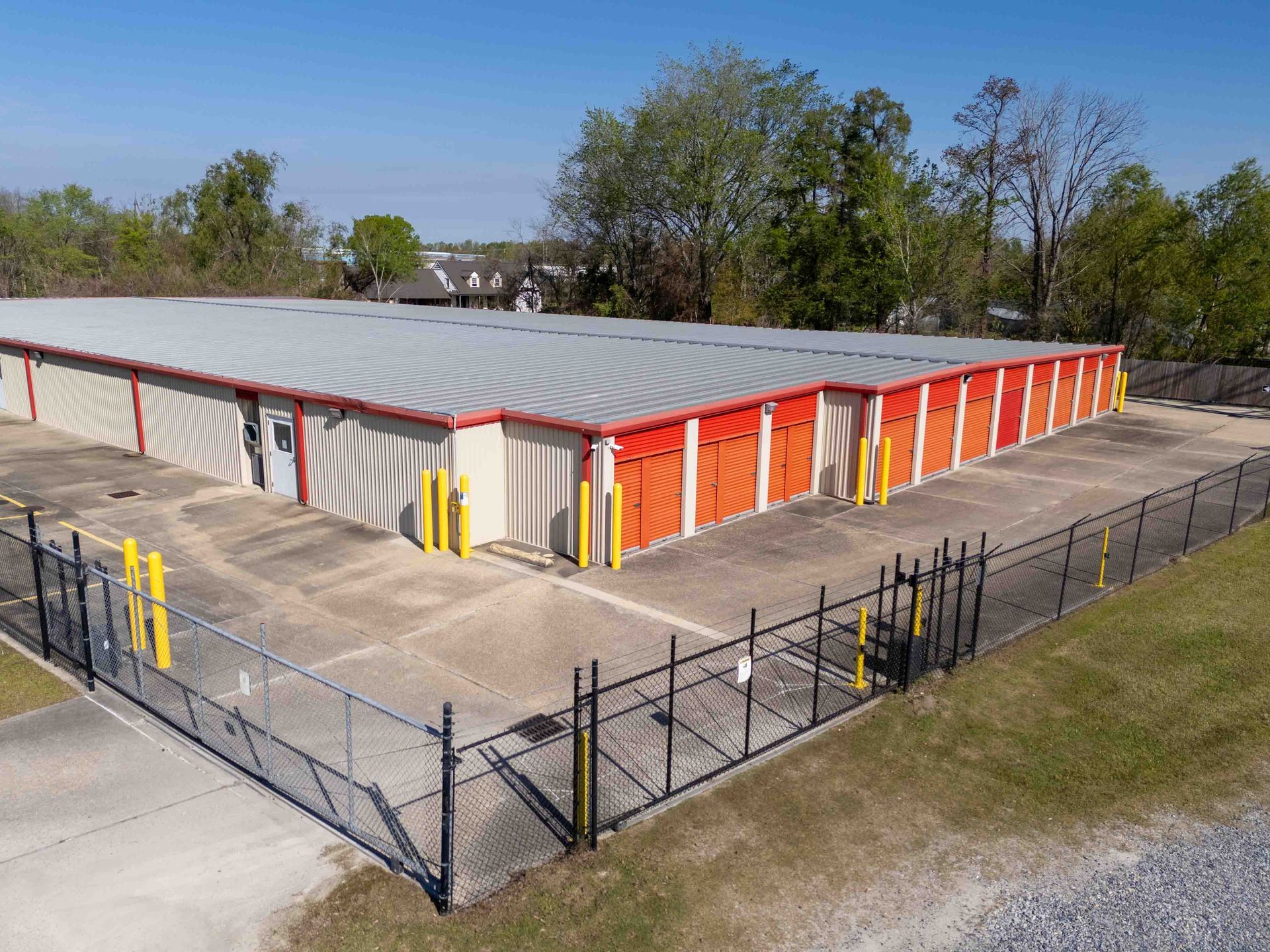 Drive-up storage units with orange doors behind a gated, fenced lot at Premier Storage & Shipping in Addis, LA