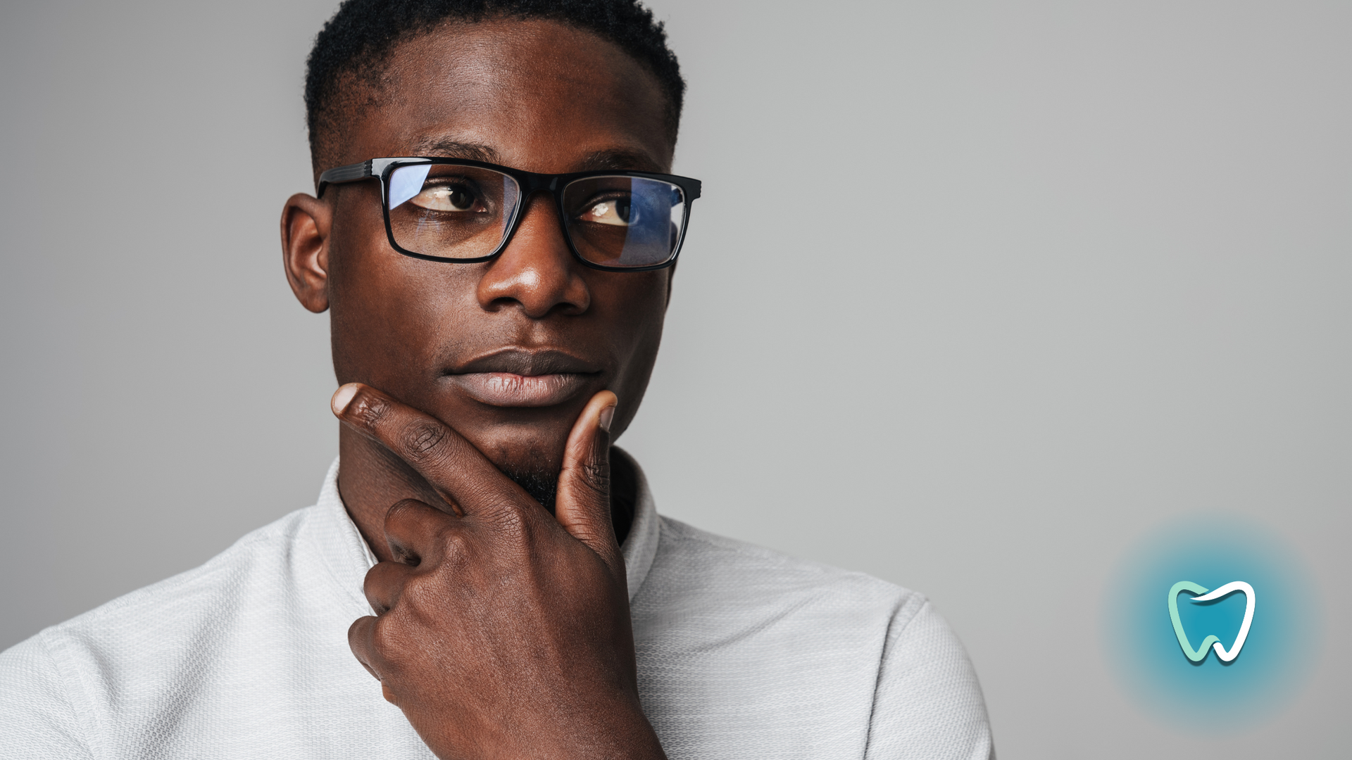 A man wearing glasses is holding his hand to his chin.