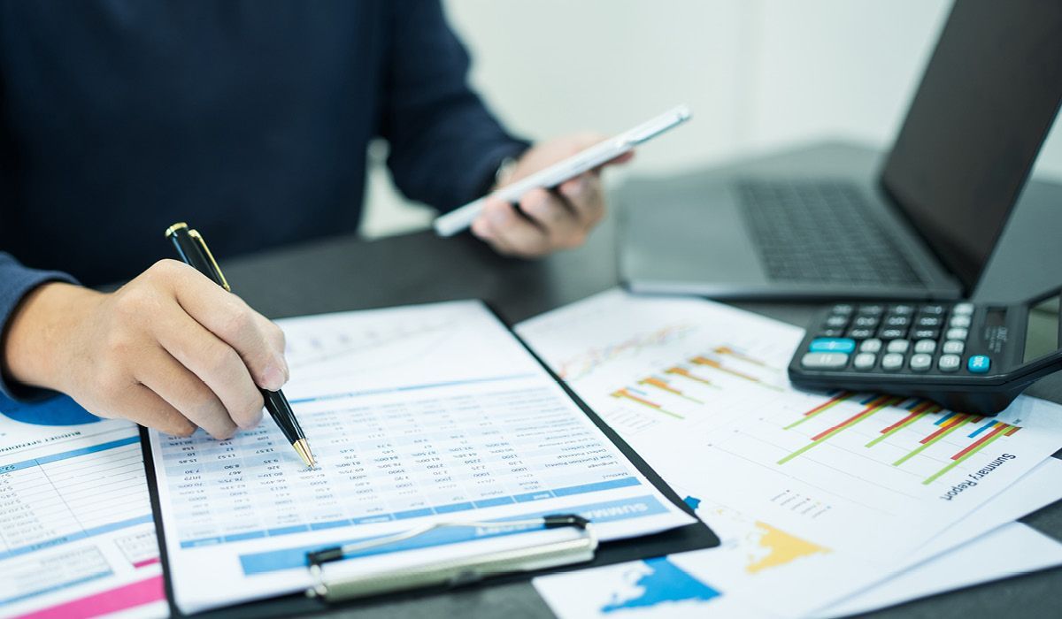Person reviewing financial charts at a desk with a calculator, clipboard, and smartphone nearby