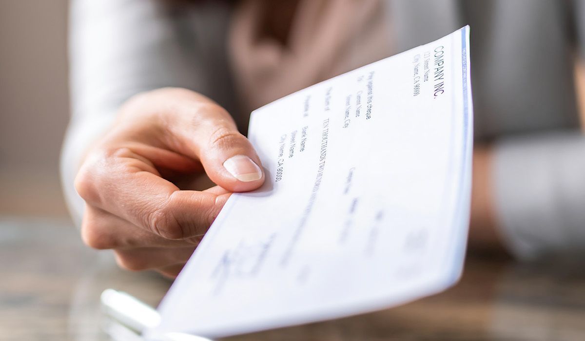 Hand holding a white document or check in a blurred indoor setting