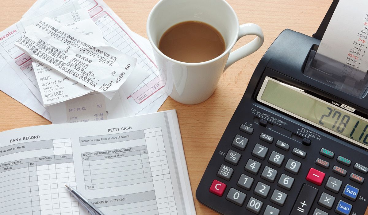 Calculator, coffee cup, and receipts on a desk with bills and paperwork.