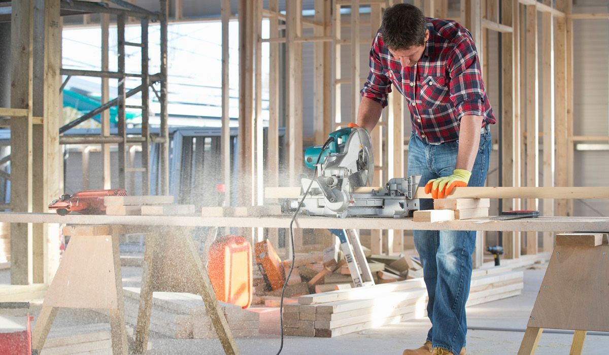 Worker in red plaid shirt cutting lumber with a circular saw at a construction site