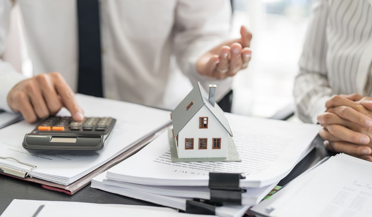 Hands using calculator beside house model and paperwork during a home finance discussion